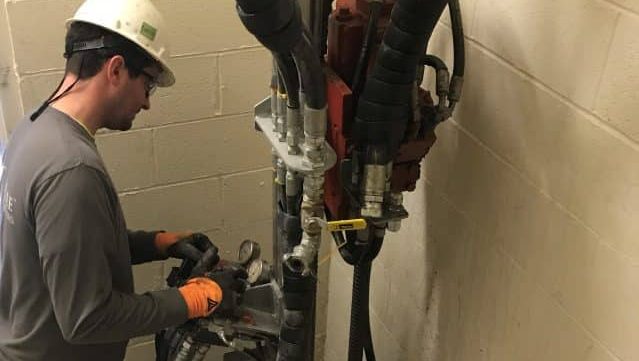 Operator using a TEI man portable drill rig in a tight interior stairwell corner to install micropiles on a confined‑space foundation project.