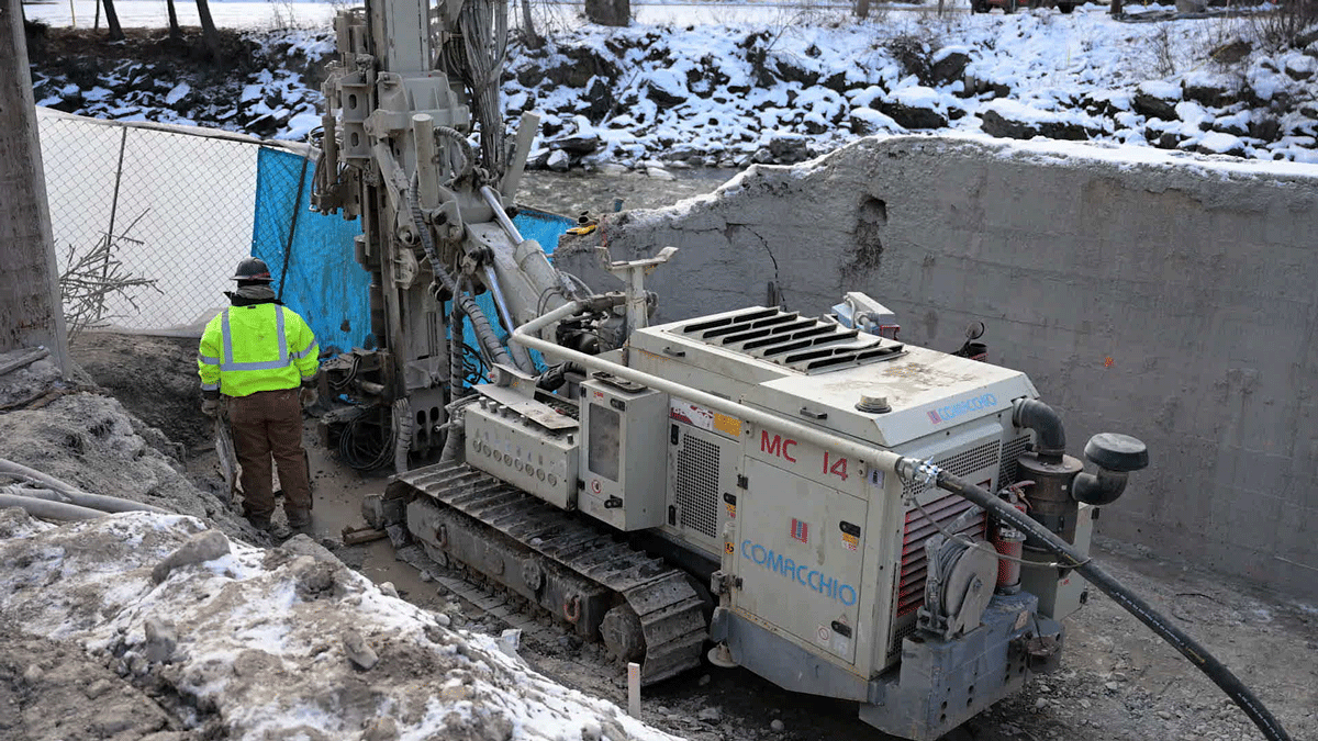 Close‑up of the Comacchio MC 14 fully articulated microdrilling rig’s crawler base, power pack, and control console on a cold, muddy jobsite, highlighting the compact footprint and rugged undercarriage that make the MC 14 ideal for confined micropile and anchor projects.