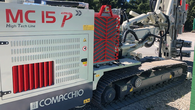 Comacchio MC 15P multipurpose drill rig side detail showing engine enclosure, tracks, and fully articulated mast system parked on a gravel yard.