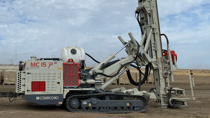 Comacchio MC 15P fully articulated multipurpose drill rig on tracks with mast raised on a remote project site under a cloudy sky.