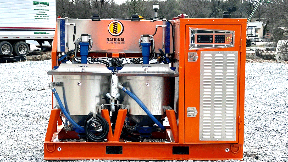 Bright orange INTRIC D9 colloidal grout plant from National Piling Products sitting on gravel at a job site, showing twin stainless steel mixing tanks, blue pumps, and enclosed control cabinet.