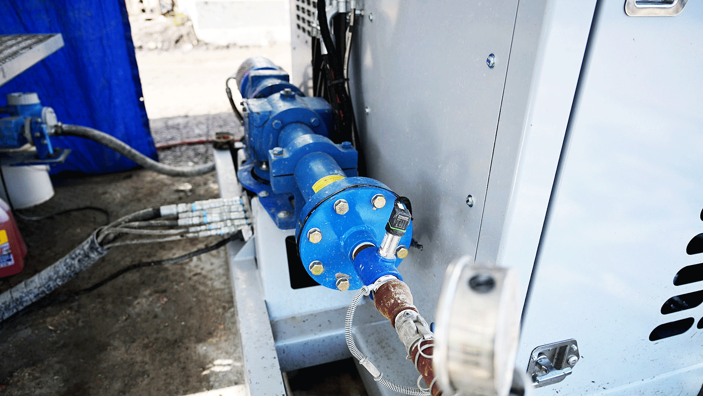 Blue progressive cavity pump mounted on the side of an Intric PS‑300 pump station, with hydraulic hoses and fittings connected for grout pumping operations on a construction site.
