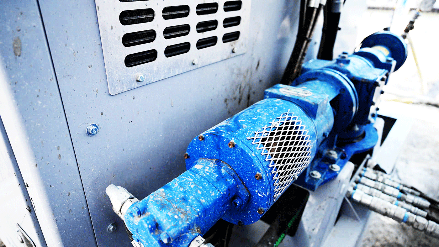 Close-up of the blue progressive cavity pump and guarded drive section mounted on the Intric PS‑300 pump station, with hydraulic hoses connected for grout pumping on a construction site.