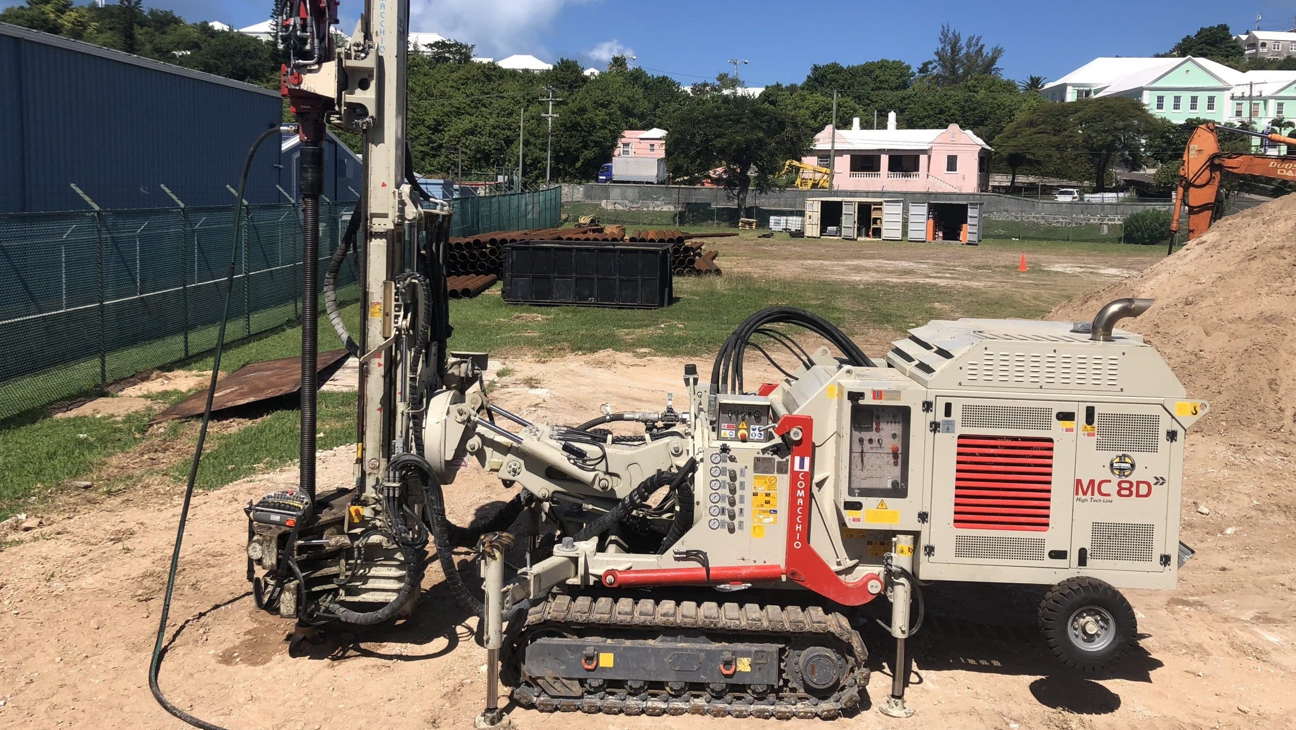 Comacchio MC8D track drill rig set up on a sandy jobsite near colorful coastal buildings, drilling foundations on a sunny day.