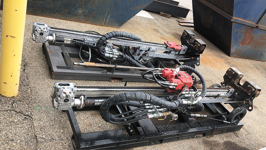 Two TEI MP260 man‑portable drill systems resting on steel pallets, showing the feed rails, rotary drill heads, red hydraulic manifolds, and bundled hoses arranged on a concrete yard, proudly made in the USA.