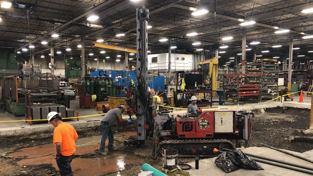 TEI TD‑100 electric‑hydraulic limited‑access drill rig installing interior micropiles inside an active industrial facility with National Piling Products crew.