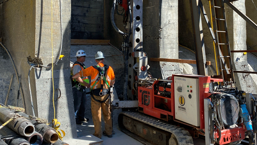 TEI TD‑100 electric‑hydraulic limited‑access drill rig working between tall concrete walls with crew preparing for vertical micropile drilling.