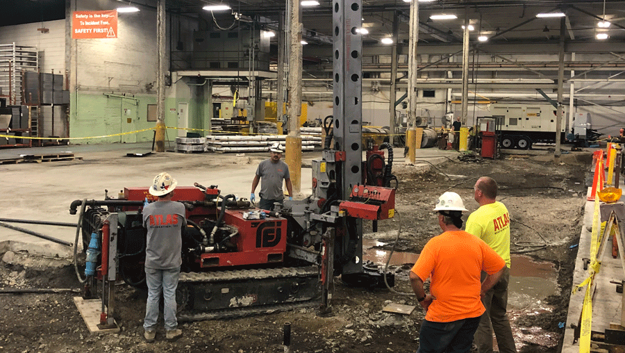 TEI TD‑100 electric‑hydraulic limited‑access drill rig drilling interior micropiles with crew inside a large industrial warehouse.