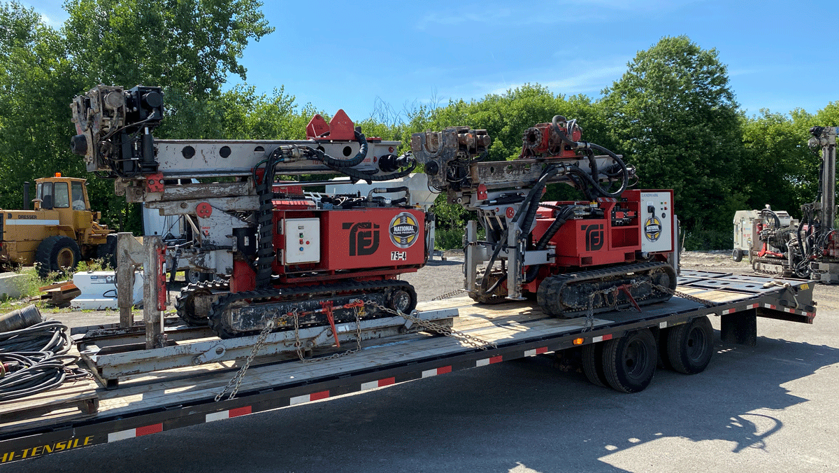 Two TEI TD‑100 electric‑hydraulic limited‑access drill rigs loaded on a trailer at National Piling Products yard, ready for mobilization.