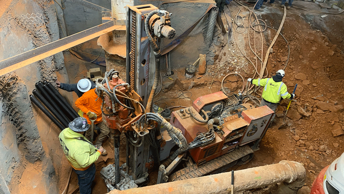 TEI TD‑100 electric‑hydraulic limited‑access drill rig installing hollow bar micropiles in a deep excavation with crew working around utilities and shoring.
