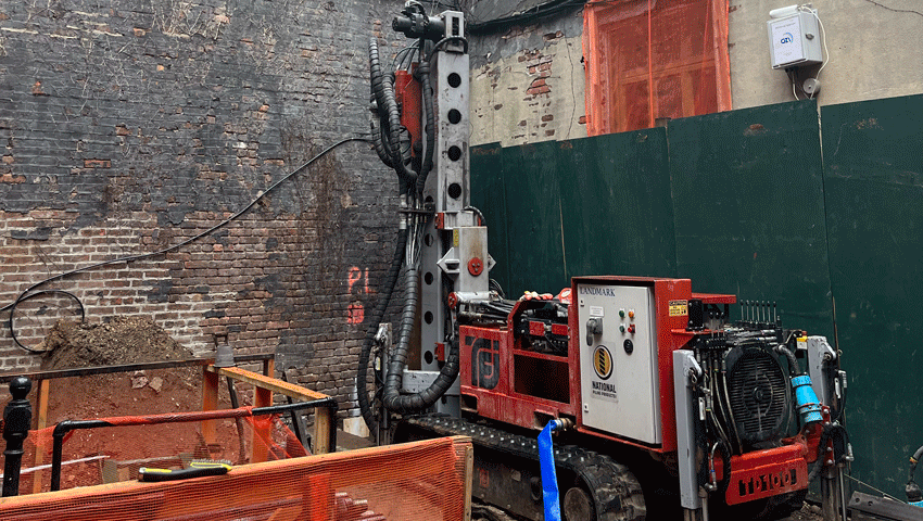 TEI TD‑100 electric‑hydraulic limited‑access drill rig set up in a narrow urban lot, drilling micropiles beside tall masonry walls.