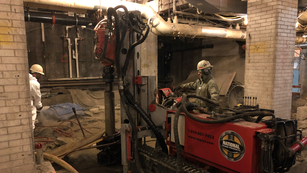 TEI TD‑75 electric‑hydraulic limited‑access drill rig installing a vertical micropile inside an existing building with National Piling Products operator.