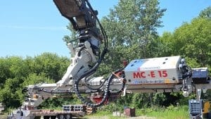 Comacchio MC‑E15 excavator drill attachment from National Piling Products extended over a jobsite, ready for confined‑access micropile drilling.