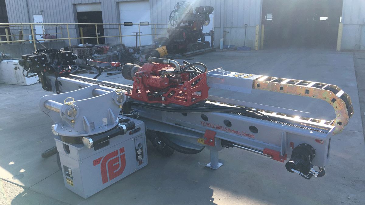 National Piling Products TEI HEM hydraulic excavator‑mounted drilling attachment staged in the yard, showing the mast, drifter, and hydraulic rotation head.