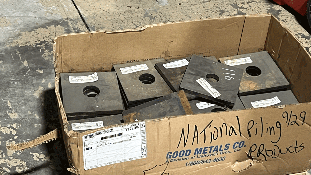 Box of hollow bar bearing plates for sale from National Piling Products on a shop floor.