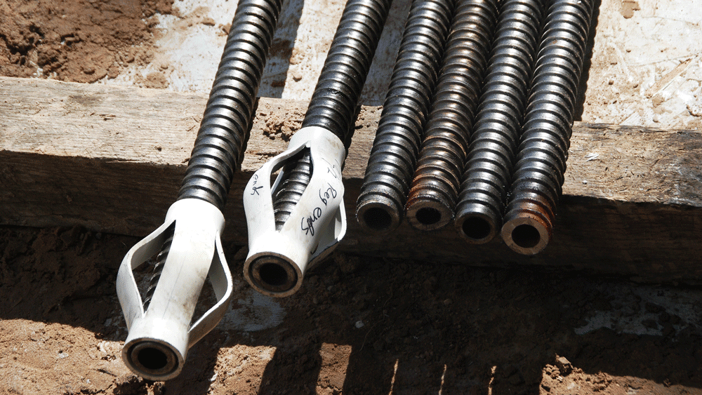 Self‑drilling hollow bar anchors with couplers laid out on a jobsite next to soil and formwork.