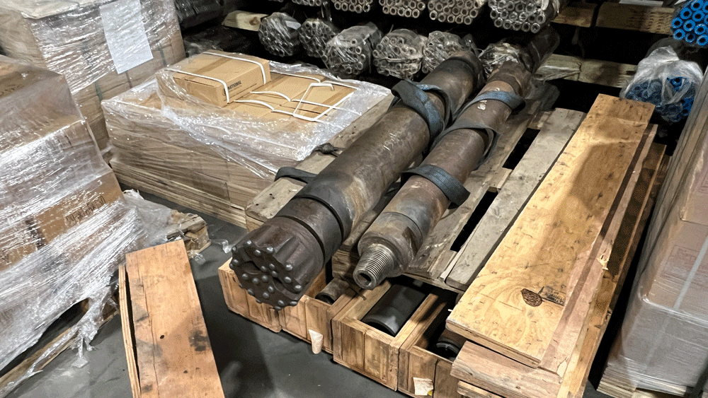 Large custom drilling tools and hammer assemblies stored on a pallet in the National Piling Products warehouse.