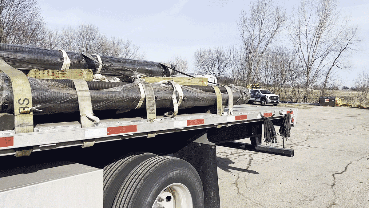 Wrapped hollow bar micropile bundles strapped to a flatbed trailer at National Piling Products yard.
