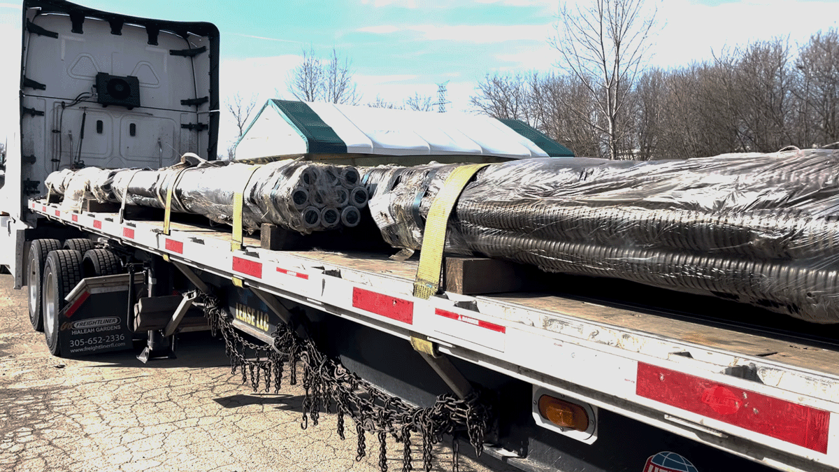 Flatbed trailer loaded with wrapped hollow bar micropile bundles secured with straps for delivery from National Piling Products.